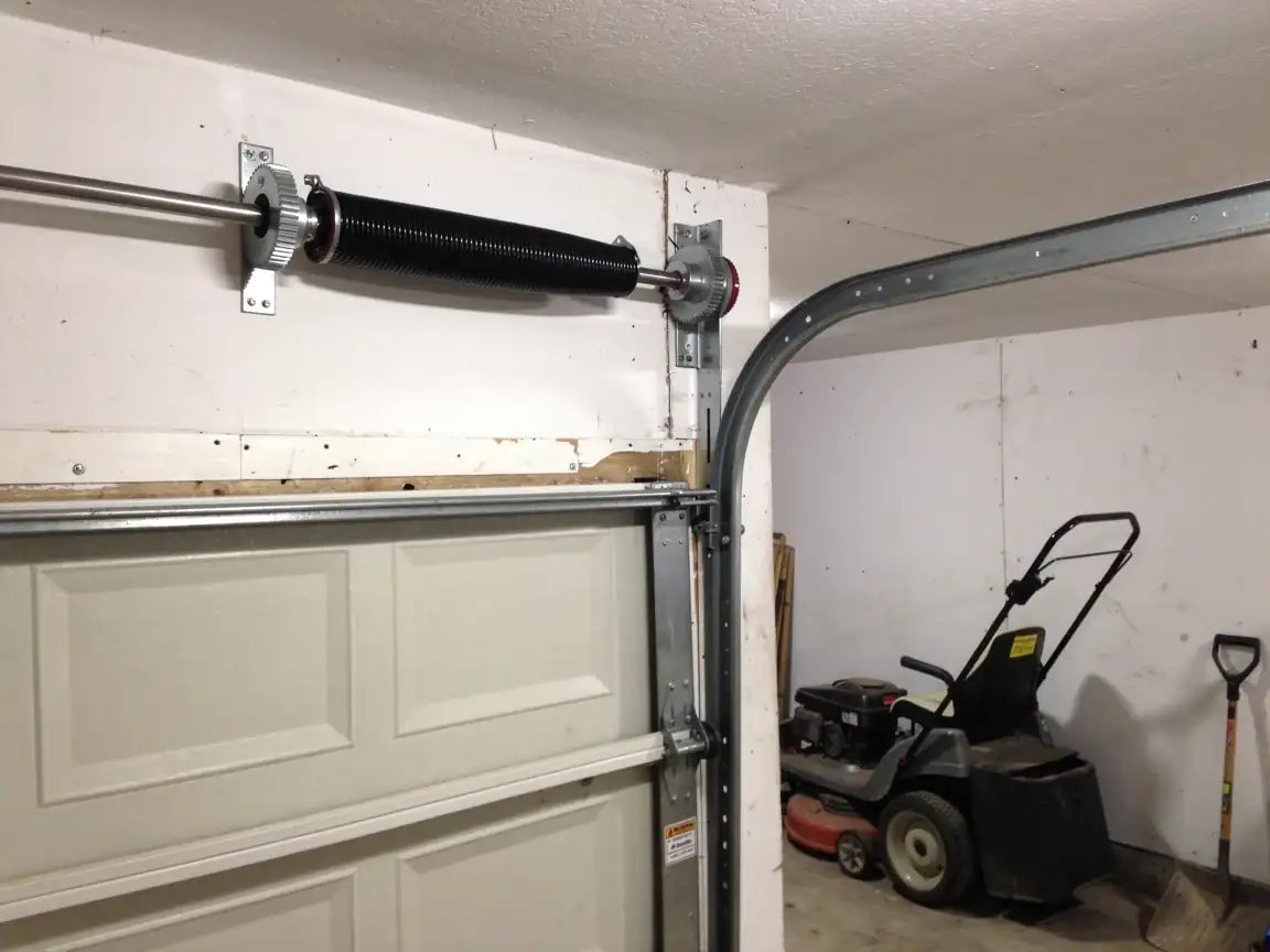 A black torsion spring is mounted above a white garage door.
